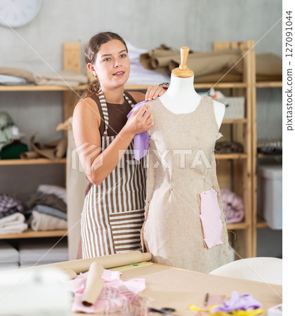Female tailor sews new dress on a mannequin in sewing studio 127091044