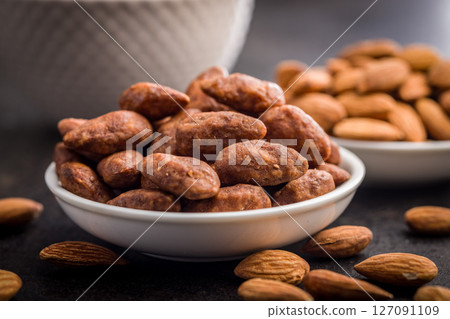 Almond nuts coated in sugar and honey in bowl on black table. 127091109