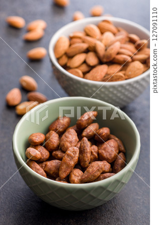 Almond nuts coated in sugar and honey in bowl on black table. Almond nuts coated in sugar and honey in bowl on black table. 127091110