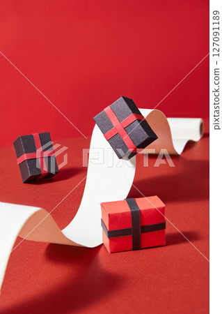Floating paper gift boxes and elegant ribbon shapes on red background. Dynamic layout with shadows expresses a sense of motion and shopping excitement 127091189