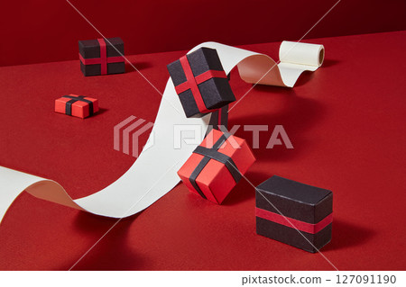 A vibrant paper setup with spiral ribbons and hanging gift boxes on a red background. A creative metaphor for holiday shopping sprees and big sales A vibrant paper setup with spiral ribbons and hanging gift boxes on a red background. A creative metaphor for holiday shopping sprees and big sales 127091190