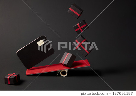 Gift boxes and ATM cards are playing seesaw on minimalist black background. Represents online orders, digital sales or festive e-commerce delivery. 127091197