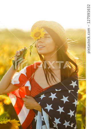 Beautiful girl in hat with the American flag in a sunflower field. 4th of July. Fourth of July. Freedom 127091632