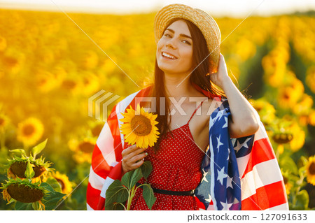 Beautiful girl in hat with the American flag in a sunflower field. 4th of July. Fourth of July. Freedom 127091633