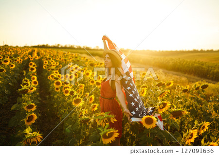 Beautiful girl in hat with the American flag in a sunflower field. 4th of July. Fourth of July. Independence Day. 127091636
