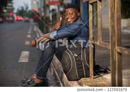 young man happy traveler sitting in the street waiting for a car 127091679