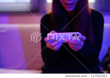 Young woman excited while playing mobile game with vibrant colored lighting Young woman excited while playing mobile game with vibrant colored lighting 127091952
