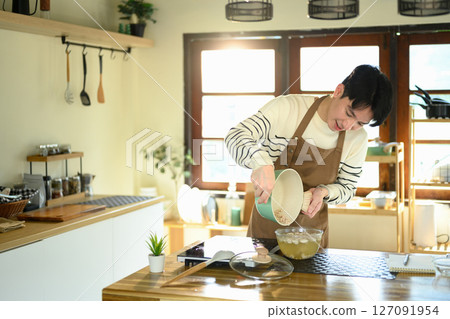 Cheerful man wearing apron finishing up meal prep with care and attention 127091954