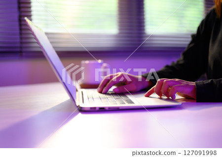 Close up of hands typing on a laptop under ambient purple lighting Close up of hands typing on a laptop under ambient purple lighting 127091998