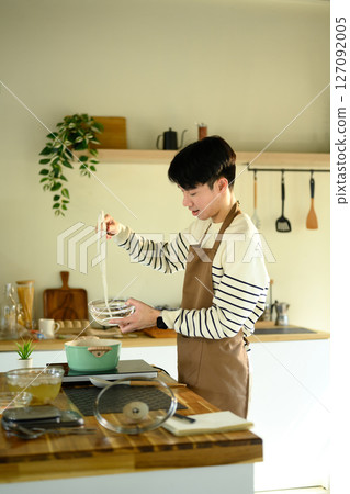 Smiling man in apron preparing noodles in a cozy home kitchen Smiling man in apron preparing noodles in a cozy home kitchen 127092005