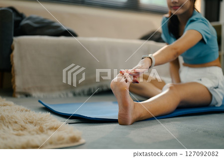 Focused shot of a woman doing a seated hamstring stretch on a yoga mat Focused shot of a woman doing a seated hamstring stretch on a yoga mat 127092082