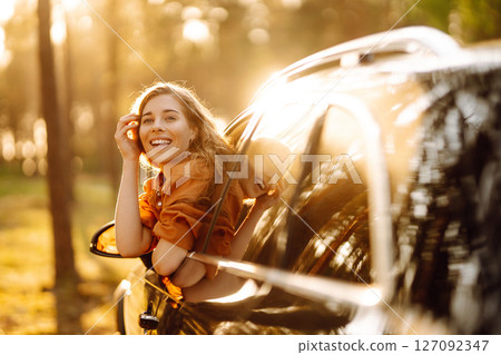 A young woman feels freedom leaning out of a car window in a sunny forest. Travel concept. 127092347