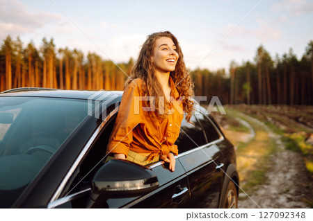 A young woman feels freedom leaning out of a car window in a sunny forest. Travel concept. 127092348