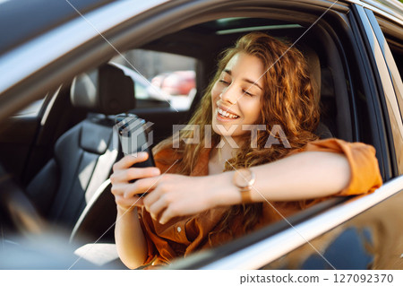 Happy woman in the car in the driver's seat looks at the smartphone. Business, technology concept. Happy woman in the car in the driver's seat looks at the smartphone. Business, technology concept. 127092370