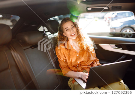 Business beautiful woman with modern laptop sits in back seat of car. Successful startup. 127092396