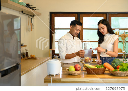Young couple preparing a healthy smoothie together in a cozy home kitchen Young couple preparing a healthy smoothie together in a cozy home kitchen 127092975