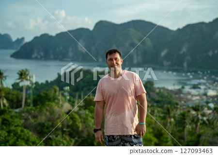 A guy in a pink wet T-shirt stands against the backdrop of the island of Pi Pi Don 127093463