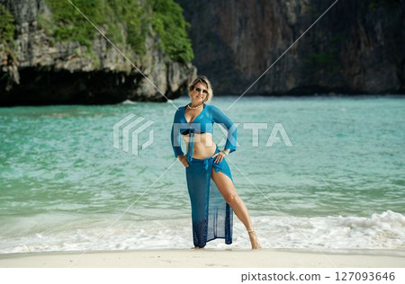 Woman in blue beach dress and flower in hair standing on wild green beach 127093646