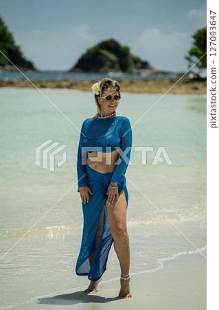 A woman wearing a blue bikini and a flower in her hair stands on a beach A woman wearing a blue bikini and a flower in her hair stands on a beach 127093647