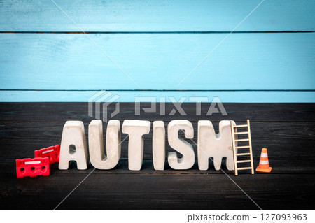 AUTISM. Concrete alphabet letters on a blue and black wooden background AUTISM. Concrete alphabet letters on a blue and black wooden background 127093963