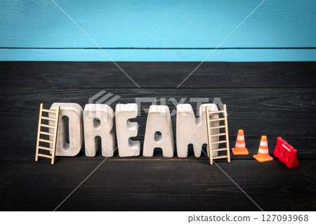 DREAM. Concrete alphabet letters on a blue and black wooden background DREAM. Concrete alphabet letters on a blue and black wooden background 127093968