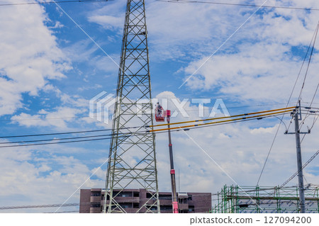 A man working near a high-voltage tower on a work platform 127094200