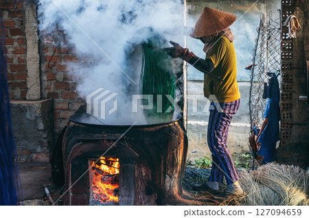 Vietnamese female worker works in a cane dyeing workshop at a wicker mat factory in a village in Vietnam 127094659