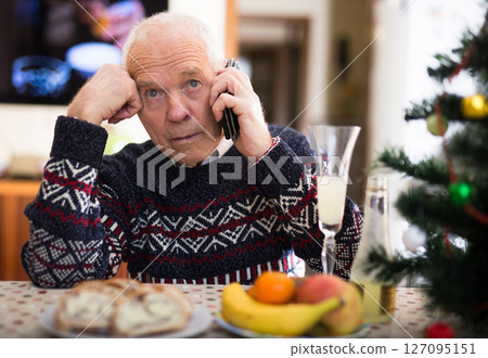 Upset older man talking on phone at table during New Year celebration Upset older man talking on phone at table during New Year celebration 127095151