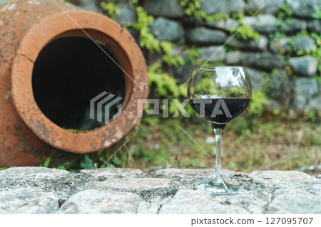 Glass of Red Wine with Traditional Georgian Qvevri in Rustic Setting 127095707