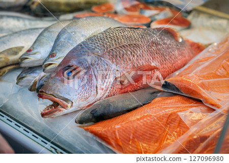 Close-up of various fresh fish and salmon fillets displayed on ice, seafood market. Sale of fresh frozen fish. Open showcases of seafood market. Concept of fresh fish, seafood selection, healthy diet 127096980