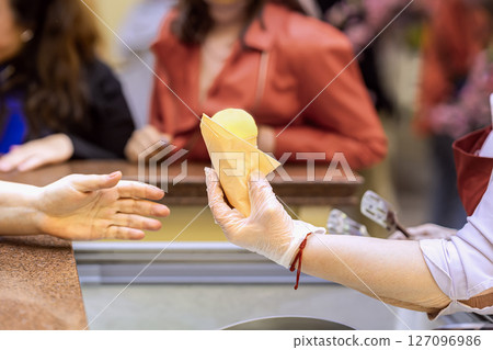 Ice cream seller giving ice cream cone to customer. Vendor in glove handing yellow ice cream cone to customer across counter. Concept of ice cream, food service, organic summer refreshment Ice cream seller giving ice cream cone to customer. Vendor in glove handing yellow ice cream cone to customer across counter. Concept of ice cream, food service, organic summer refreshment 127096986