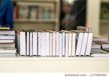 Stack of hardcover books lined up on white shelf in bookstore environment. Concept of books, reading habits, literature, publishing 127096988