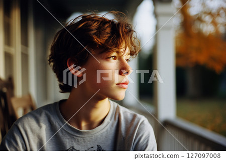 A boy with brown hair is sitting on a porch 127097008