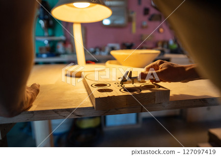 Craftsman using calipers on lamp templates in workshop. Handmade blueprints, unique lighting design 127097419