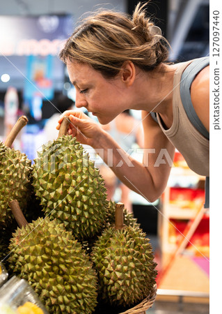 Woman cautiously sniffs durian on counter. Tropical exotic fruit choosing during grocery shopping Woman cautiously sniffs durian on counter. Tropical exotic fruit choosing during grocery shopping 127097440