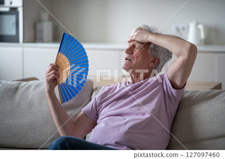 Older man struggling with fan heat exhaustion. Pensioner try to cope in sweltering home in summer Older man struggling with fan heat exhaustion. Pensioner try to cope in sweltering home in summer 127097460