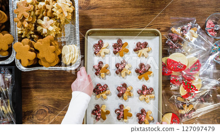 Flat lay. Carefully packaging Christmas cutout cookies, half-dipped in chocolate, sprinkled with crushed nuts, and presented in clear cellophane wrapping. 127097479