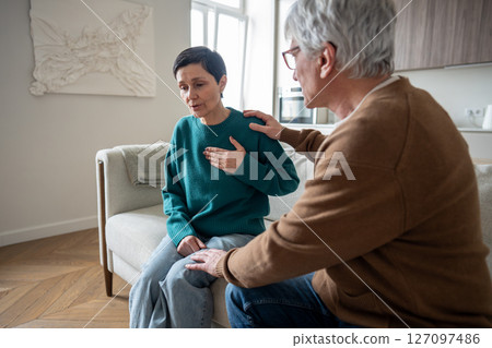 Heavily breathing woman grip chest on sofa, sudden panic attack while husband unsure how to help Heavily breathing woman grip chest on sofa, sudden panic attack while husband unsure how to help 127097486