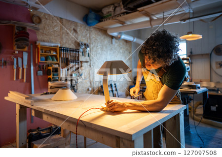 Skilled woodworker examining handmade lamp detail. Checking red wire connection, custom design diy Skilled woodworker examining handmade lamp detail. Checking red wire connection, custom design diy 127097508