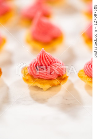 Freshly baked lemon spritz cookies with a swirl of cranberry buttercream piped on top. The vibrant pink filling contrasts beautifully with the golden cookie base, creating an elegant dessert 127097509