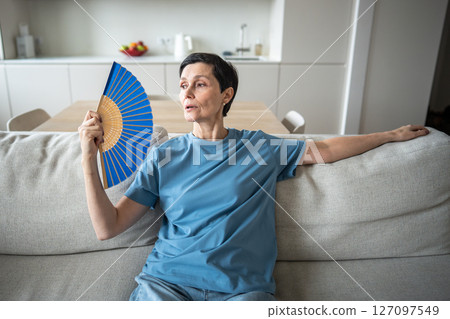 Exhausted mature woman fanning herself at home. Unbearable heat, elderly suffering from stuffy 127097549