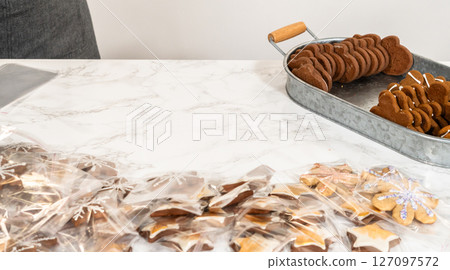 Captured from a mid-range perspective, a person carefully packages a decorated Christmas tree-shaped cookie while an assortment of festive treats, including green, red, and gingerbread cookies, is 127097572