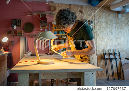 Artisan examining bent plywood lamp base carefully. Workshop quality control, original design 127097687