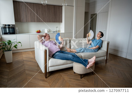 Exhausted family fan on sofa, suffocating heat exhaustion, unable breathe no air conditioning Exhausted family fan on sofa, suffocating heat exhaustion, unable breathe no air conditioning 127097711