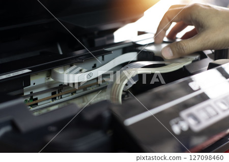 Side view of technician inspecting and repairing printer. 127098460