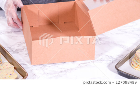 The sugar cookies, filled with sprinkles mixed into the dough, are carefully arranged with meticulous precision into a rustic brown paper box. The sugar cookies, filled with sprinkles mixed into the dough, are carefully arranged with meticulous precision into a rustic brown paper box. 127098489