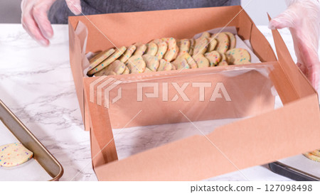 The sugar cookies, filled with sprinkles mixed into the dough, are carefully arranged with meticulous precision into a rustic brown paper box. The sugar cookies, filled with sprinkles mixed into the dough, are carefully arranged with meticulous precision into a rustic brown paper box. 127098498