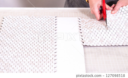 In the process of mounting peel and stick mosaic tiles onto a foam board, perfect for enhancing a food photography studio's aesthetic. 127098518