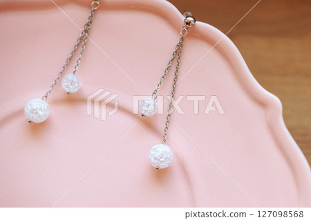Silver chain earrings with clear crackle beads on pink plate over warm wooden background 127098568