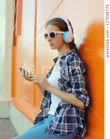 Modern young woman listening to music with smartphone, girl in headphones holding phone Modern young woman listening to music with smartphone, girl in headphones holding phone 127098778